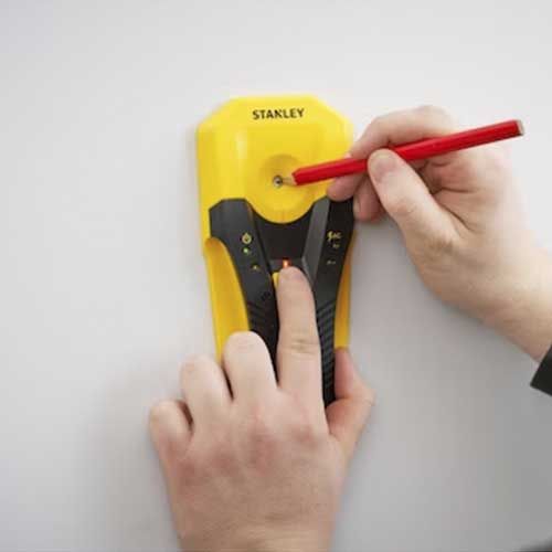 STANLEY Détecteur de matériaux stud sensor S160 - photo ambiance détecteur posé contre mur blanc avec main tenant un crayon rouge